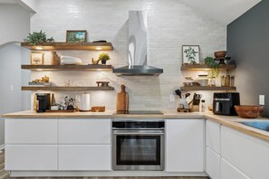 A modern kitchen with white cabinetry, a stainless steel oven, and wooden shelves with various kitchen items. - Family Friendly 3-bedroom home in Mansfield For Long Term Living - FTW 25 mins (Mansfield)