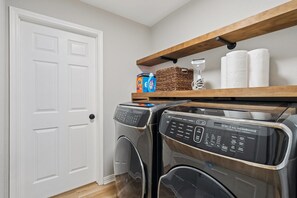 A laundry room with two front-loading washing machines, a shelf with laundry supplies, and a white door. - Family Friendly 3-bedroom home in Mansfield For Long Term Living - FTW 25 mins (Mansfield)