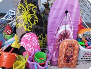 Eine Auswahl an Strandartikeln, darunter ein Surfbrett, Strandtücher und verschiedene Strandspielzeuge.