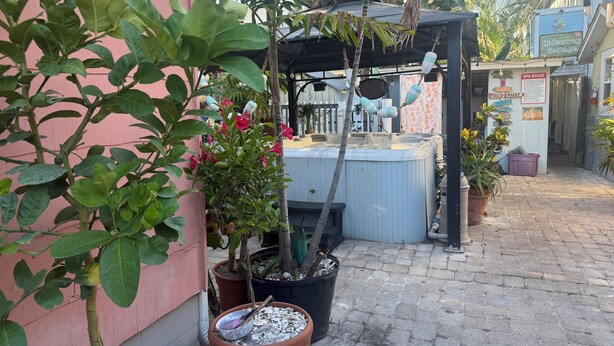 Un espace avec un jacuzzi, agrémenté d’une pergola, de plantes en pot et d’un panneau indiquant les « règles du spa ».