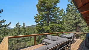 A wooden deck with a sofa and chairs, overlooking a forested area. - Lake View home 4BR 5BA gym, game room, Large kitchen (Incline Village)