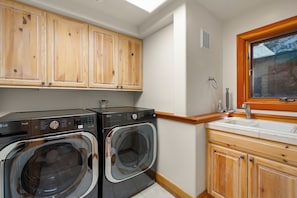 A compact laundry area with two front-loading washing machines, wooden cabinets, a sink with a wooden countertop, and a window above the sink. - Lake View home 4BR 5BA gym, game room, Large kitchen (Incline Village)