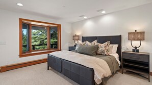 A bedroom with a large bed, two bedside tables, a window with a view of trees, and recessed ceiling lights. - Lake View home 4BR 5BA gym, game room, Large kitchen (Incline Village)