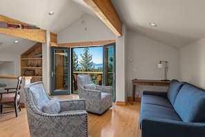 A spacious living area with a wooden ceiling, a blue sofa, patterned armchairs, a wooden table, and a view of trees and mountains through a glass door. - Lake View home 4BR 5BA gym, game room, Large kitchen (Incline Village)