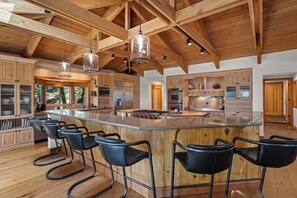 A spacious kitchen with wooden beams, a central island with bar stools, stainless steel appliances, and a view of the outdoors. - Lake View home 4BR 5BA gym, game room, Large kitchen (Incline Village)