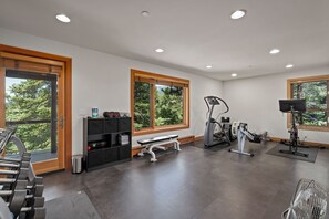 Ein Fitnessraum mit Trainingsgeräten, einer Bank und einem Fenster mit Blick auf Bäume.