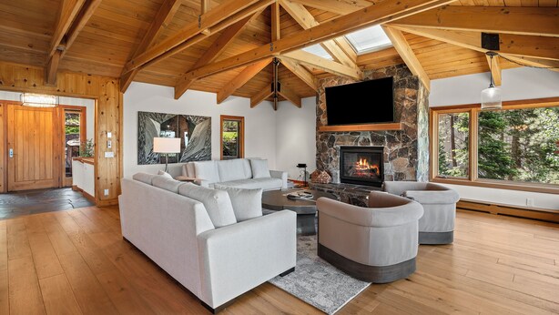 A spacious living area with a stone fireplace, wooden beams, and large windows. - Lake View home 4BR 5BA gym, game room, Large kitchen (Incline Village)