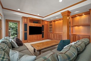 Ein geräumiges Wohnzimmer mit großem Flachbildfernseher, eingebauten Holzsäschränken und einer gemütlichen Sitzecke.