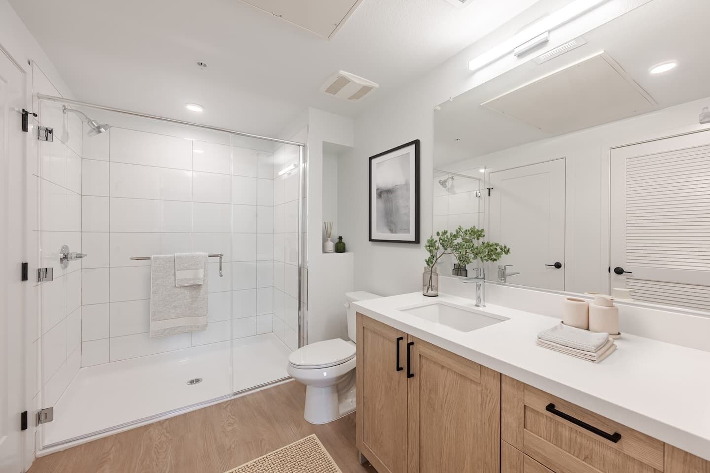A modern bathroom with a glass-enclosed shower, a toilet, a sink with a mirror, and wooden cabinets.