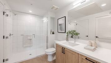 A modern bathroom with a glass-enclosed shower, a toilet, a sink with a mirror, and wooden cabinets.