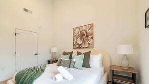 A bedroom with a bed, pillows, a blanket, a painting, and two bedside tables with lamps.