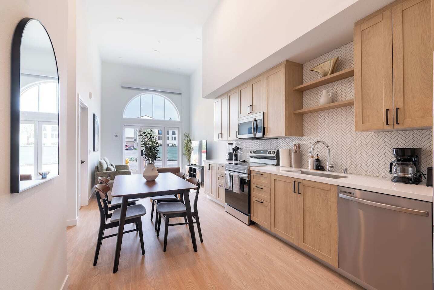Una cocina moderna con armarios de madera, electrodomésticos de acero inoxidable y un amplio ventanal que proporciona luz natural.