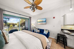 Ein Hotelzimmer mit Bett, Schreibtisch, Sessel, einem Balkon mit Blick und Deckenventilator.