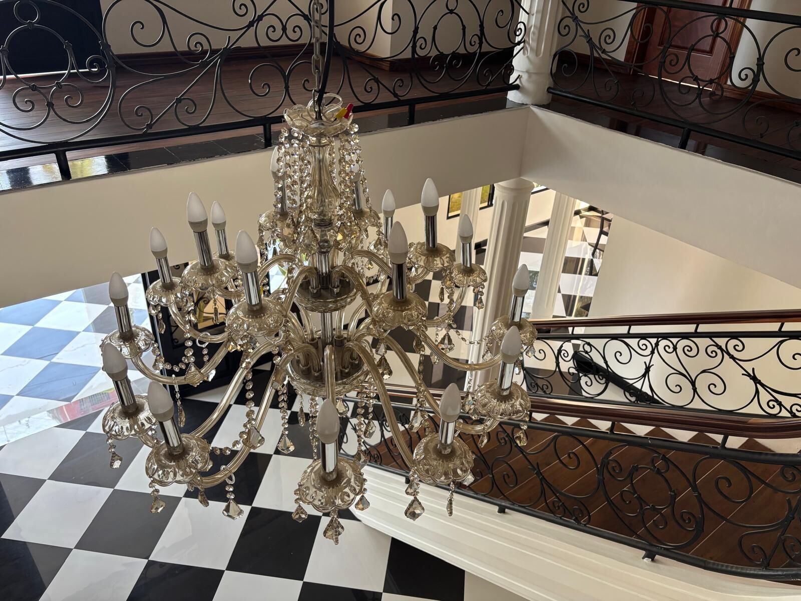 Um imponente candelabro com vários braços e detalhes em cristal, suspenso sobre um chão quadriculado.