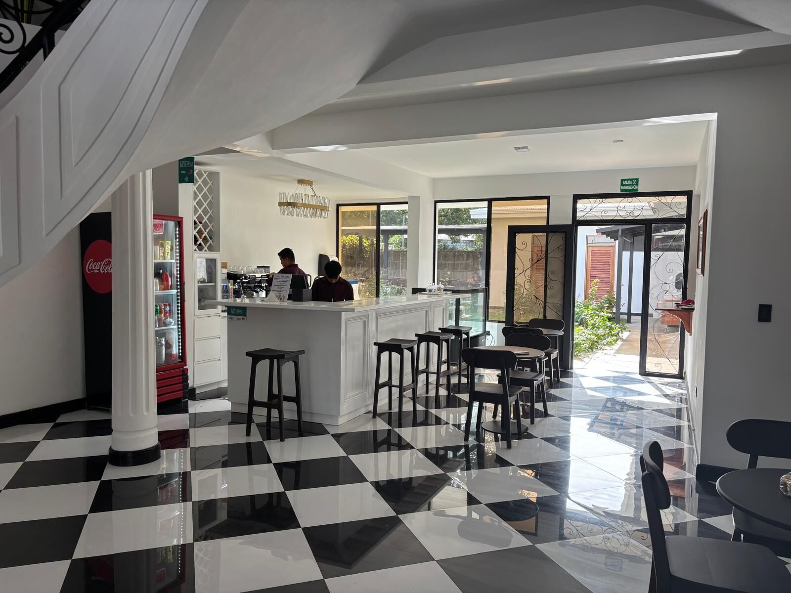 Um café moderno com piso xadrez, balcão e área de estar com mesas e cadeiras.