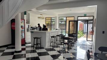 Um café moderno com piso xadrez, balcão e área de estar com mesas e cadeiras.