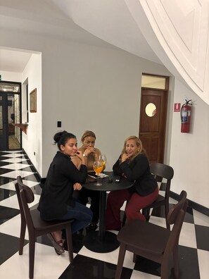 A group of people seated at a round table in a hotel lobby with a checkered floor, a fire extinguisher on the wall, and a door with a circular mirror. - Hotel San Sebastian (Diriamba)