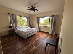 A bedroom with a bed, a chair, a ceiling fan, and large windows. - Hotel San Sebastian (Diriamba)