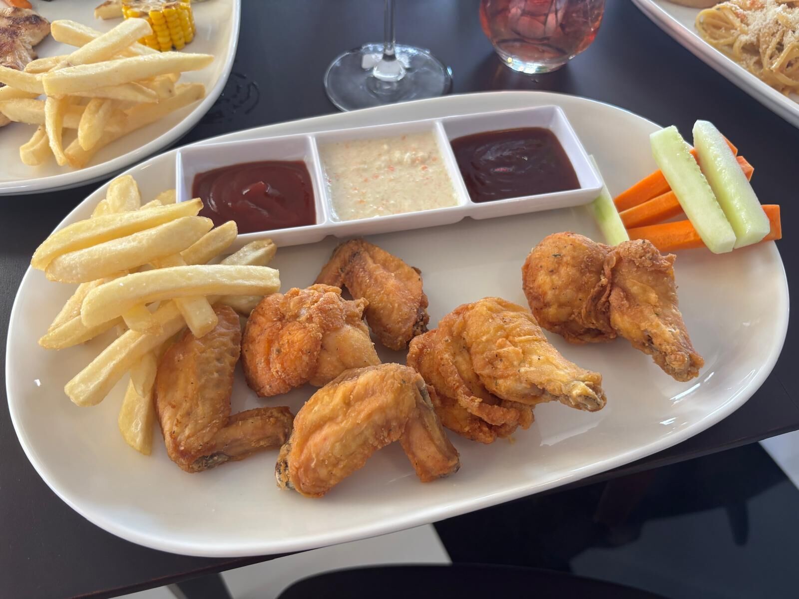 Un plato de alitas de pollo fritas, papas fritas y verduras con salsas para mojar.