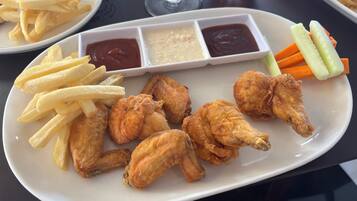 Un plato de alitas de pollo fritas, papas fritas y verduras con salsas para mojar.