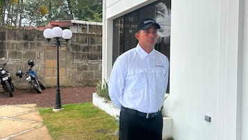 Una persona parada en un área al aire libre con diseño de cuadros, con un edificio blanco al fondo.