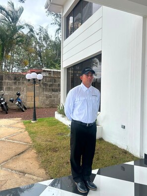 A person standing on a checkered outdoor area with a white building in the background.
