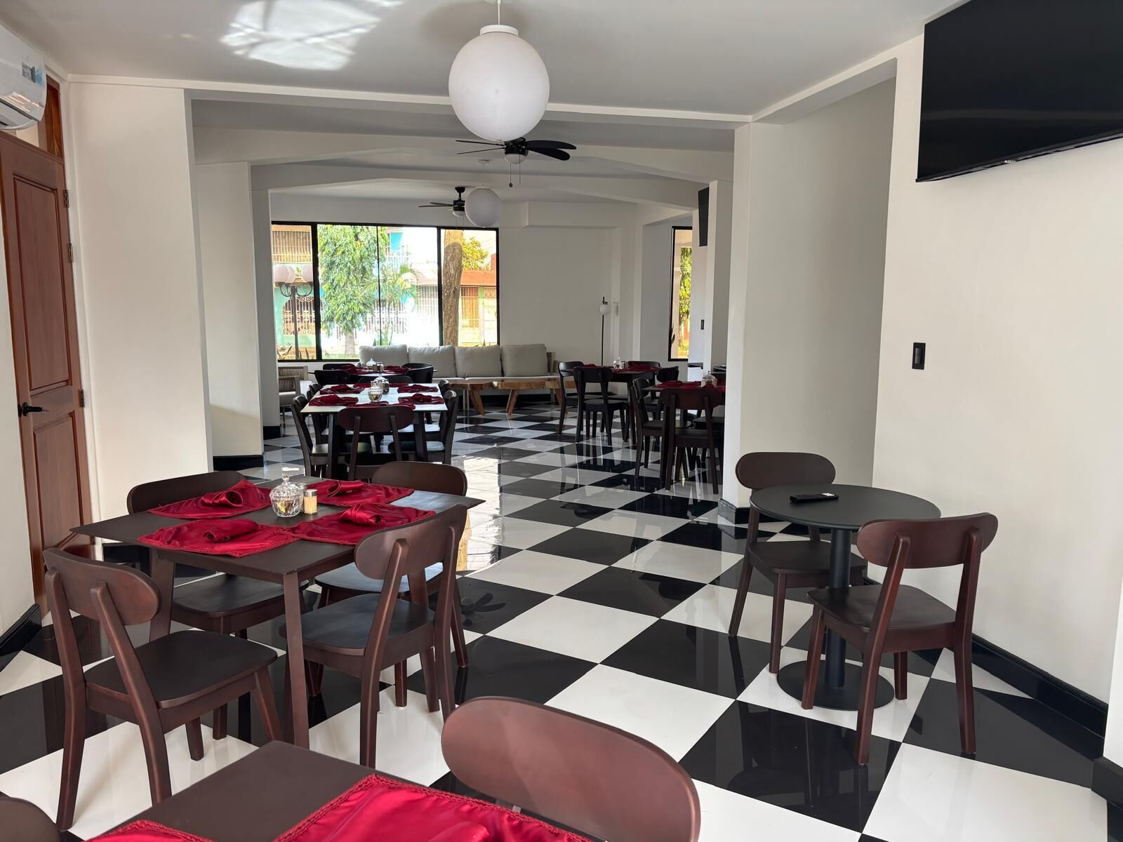 Un comedor con piso a cuadros, mesas con sillas y un ventilador de techo.