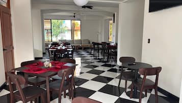 Un comedor con piso a cuadros, mesas con sillas y un ventilador de techo.