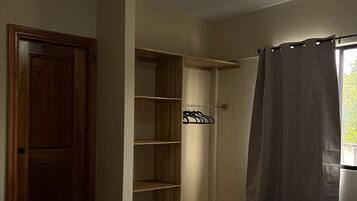 Quarto com cama, ventoinha no teto, guarda-roupa de madeira e janela com cortinas.