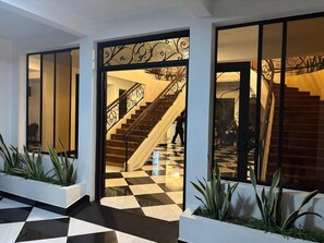 A hotel lobby with a checkered floor, a staircase with ornate railings, and potted plants. - Hotel San Sebastian (Diriamba)