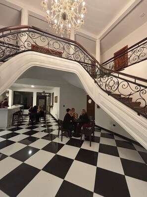 A grand staircase with ornate metal railings, a chandelier, and a checkered floor. - Hotel San Sebastian (Diriamba)