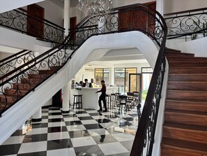 A multi-level interior with a checkered floor, a staircase with ornate metal railings, and a bar area with stools. - Hotel San Sebastian (Diriamba)