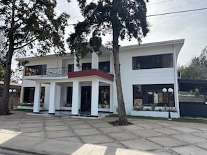 A two-story building with a balcony, a red accent wall, and a paved entrance area. - Hotel San Sebastian (Diriamba)