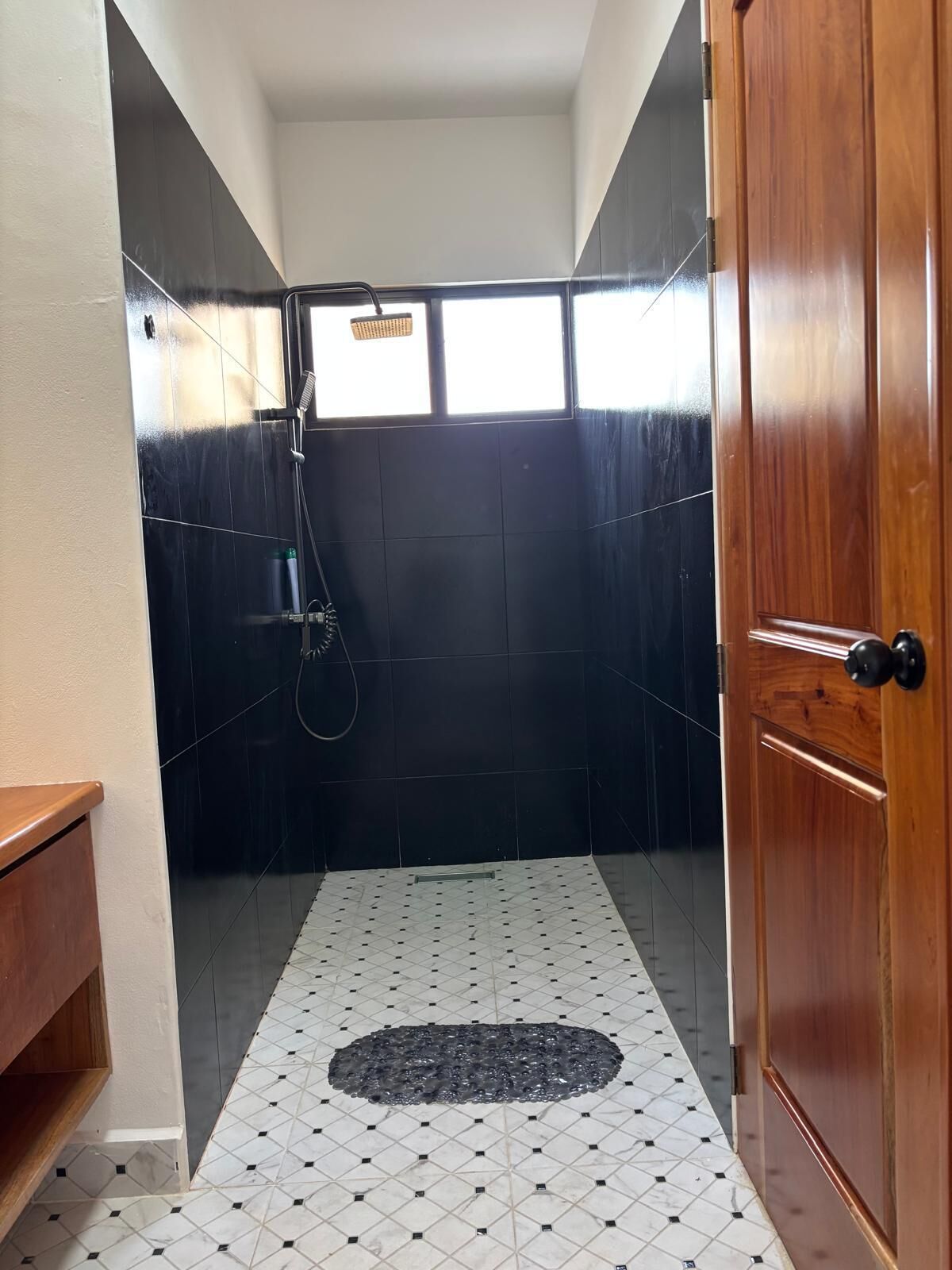 Un baño con ducha, una puerta de madera y piso de baldosas.