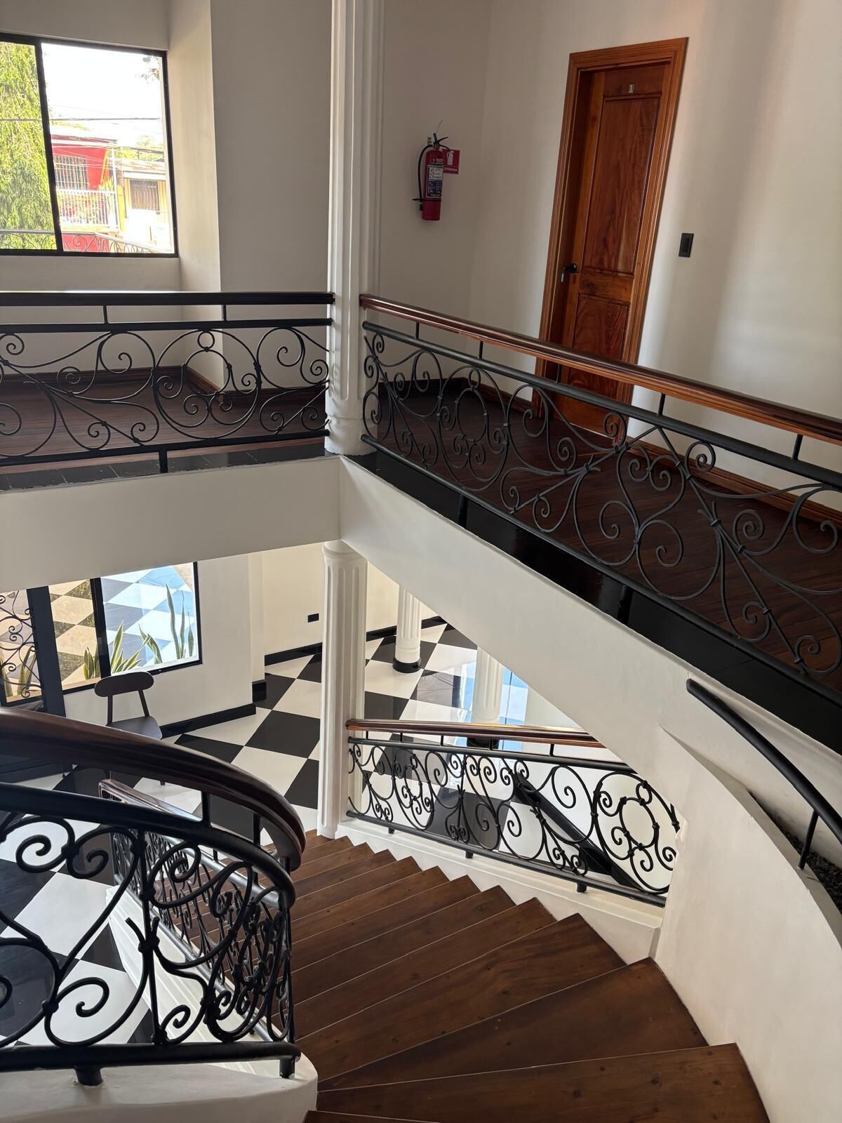 Un interior de varios niveles con una escalera, piso a cuadros blanco y negro, y una puerta de madera.