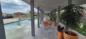 A covered outdoor area with a pool, seating, and potted plants.