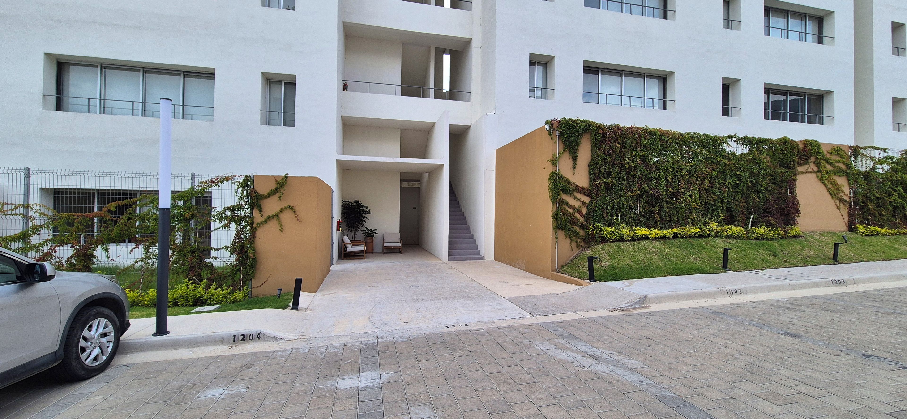 A modern building with a central staircase, a covered entrance, and a car parked in front.