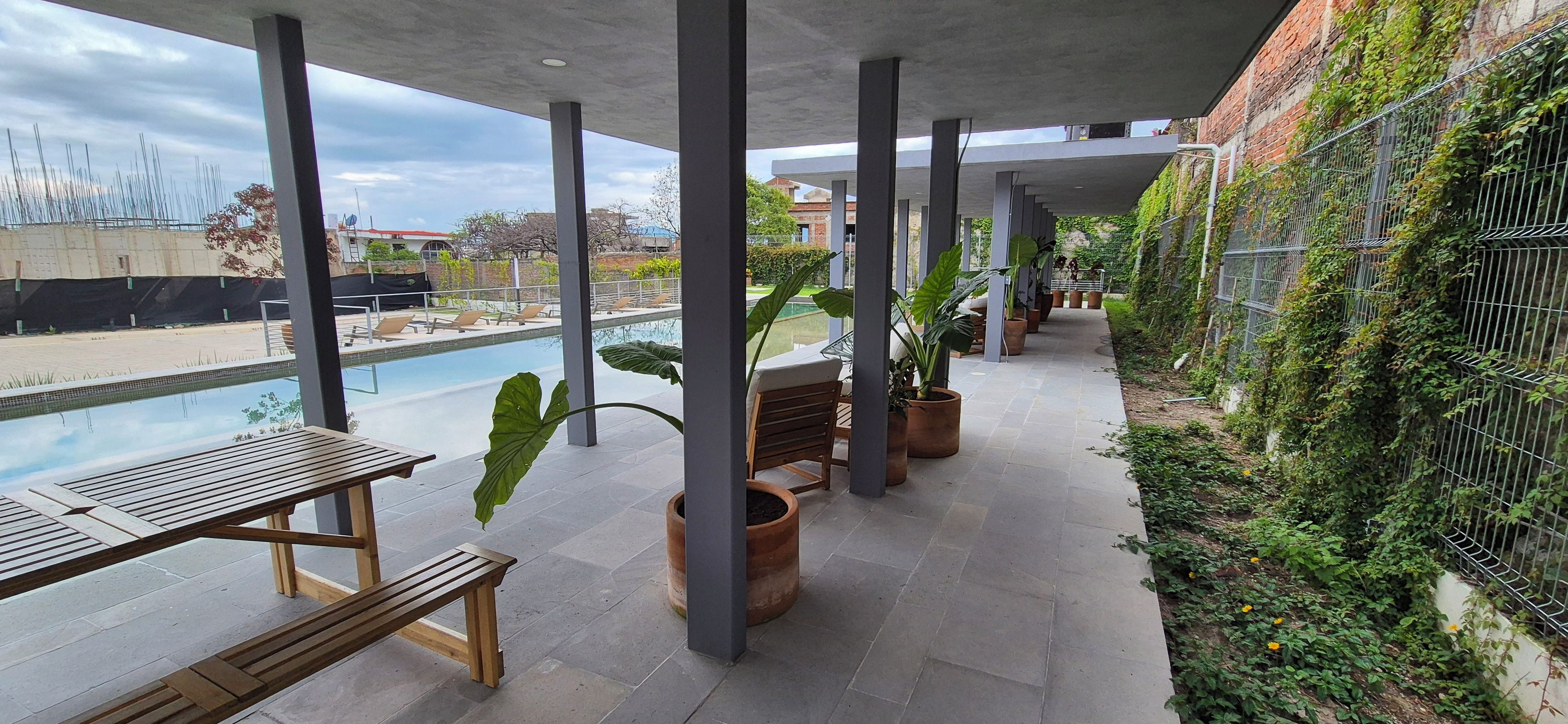 Un espace piscine extérieur doté d’un coin salon abrité, de bancs et de plantes en pot.