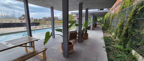 Un espace piscine extérieur doté d’un coin salon abrité, de bancs et de plantes en pot.