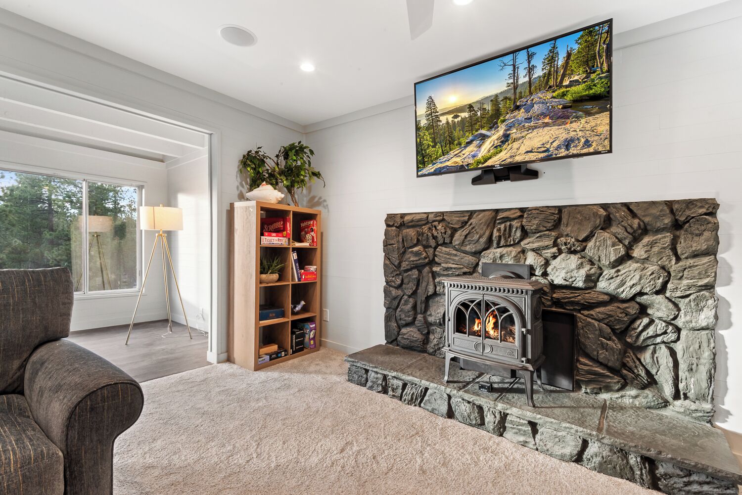 Una sala de estar con chimenea de piedra, un televisor montado encima y una estantería con varios objetos.