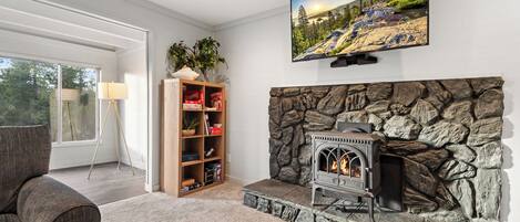 Una sala de estar con chimenea de piedra, un televisor montado encima y una estantería con varios objetos.