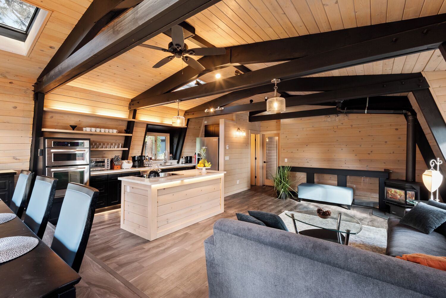 Eine moderne Küche mit Kochinsel, ein Essbereich mit Tisch und Stühlen sowie ein gemütlicher Wohnbereich mit Sofa und Kamin.