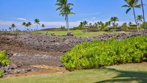Ein Golfplatz mit Lavafeld, Palmen und blauem Himmel.