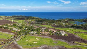 A golf course with a view of the ocean, surrounded by residential buildings and palm trees.