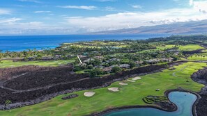Un campo de golf con vista al océano y una zona residencial con casas y palmeras.