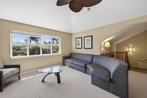 A living room with a sofa, a glass coffee table, and a view of palm trees through large windows. - 🌴 Hale Kolepa | AC | Located By Mauna Lani Golf Course 🌴 (Waimea)