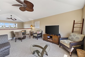 A living room with a ceiling fan, a flat-screen TV, and a dining area with chairs and a table.