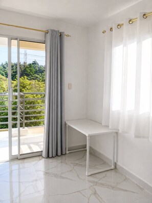 Una habitación con una mesa blanca, cortinas grises y vistas al verdor exterior.