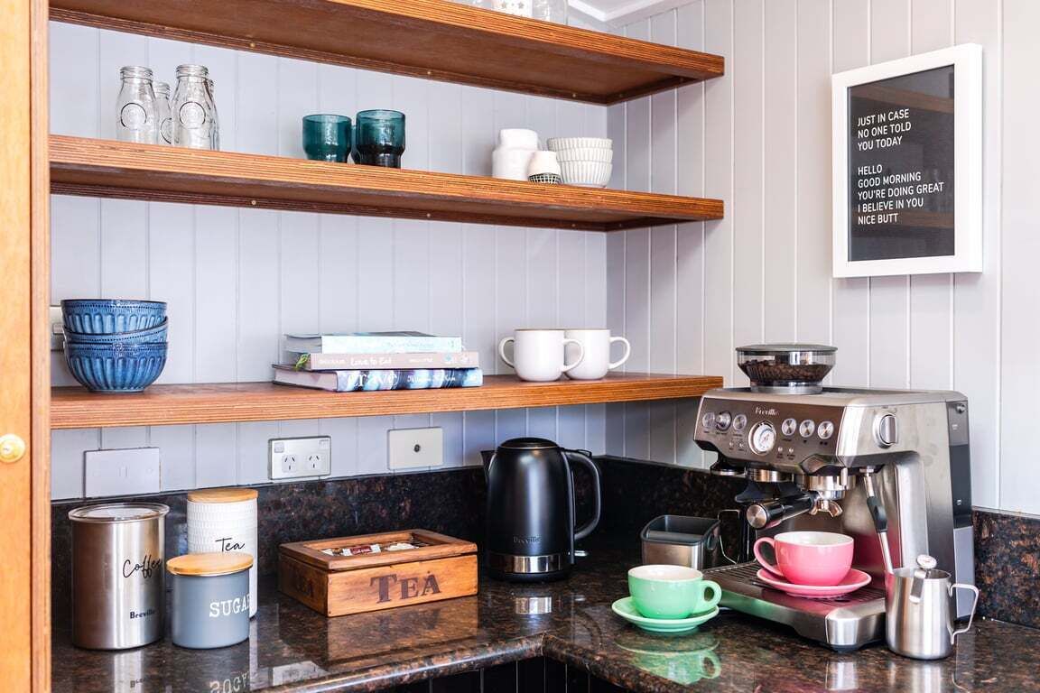 A kitchen with a coffee machine, tea containers, and a shelf with cups and books.