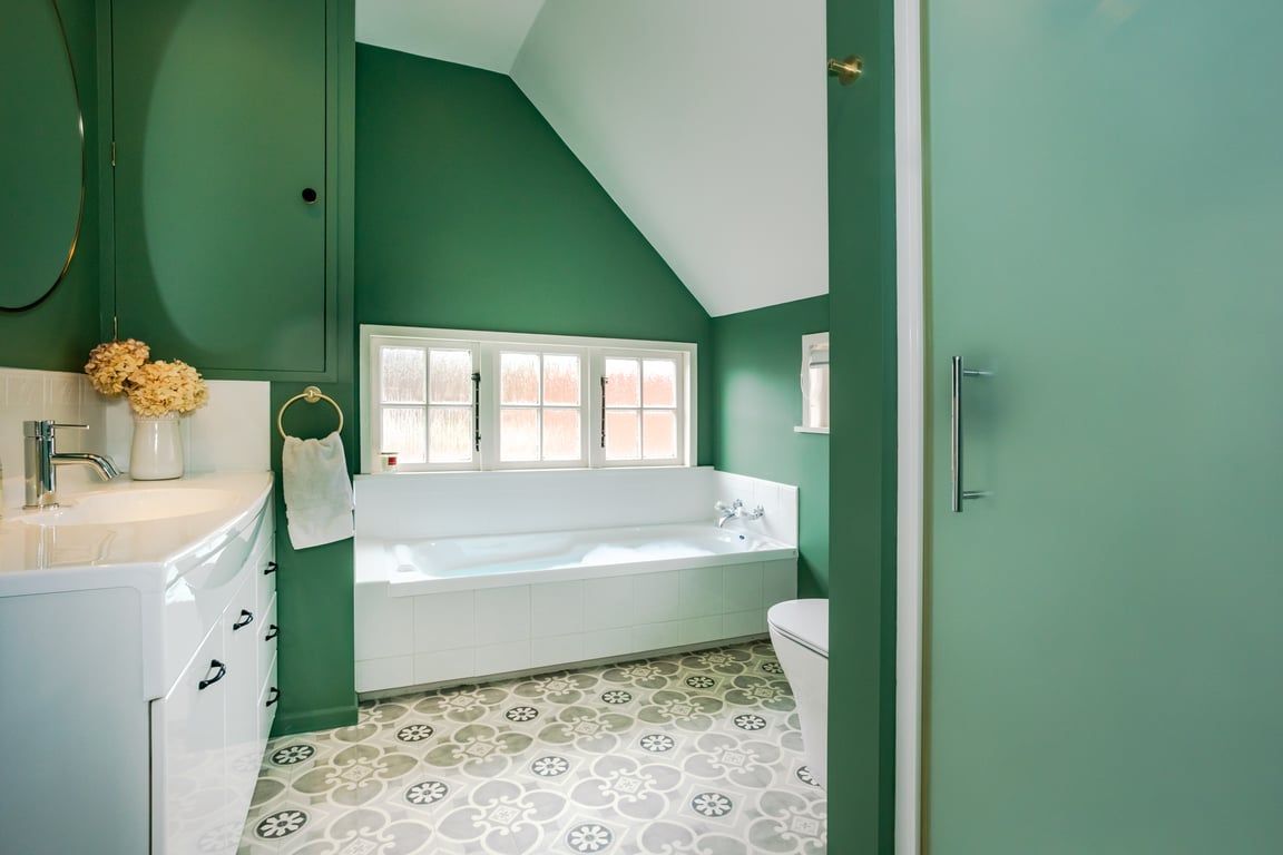 A bathroom with a white bathtub, a toilet, and a window with frosted glass.